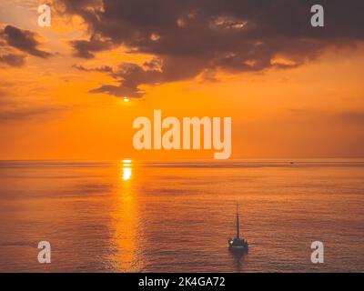Leuchtend orange Sonnenuntergang Himmel über Meer und Yacht Boot. Dramatischer Wolkenhimmel, goldene Stunde. Schöne romantische szenische Bild der atemberaubenden Seestücke. Natur Hintergrund. Sommerurlaub, Reise, Abenteuer-Konzept Stockfoto