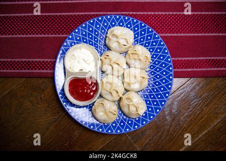 manti und Sauce auf einem blauen Teller Draufsicht Stockfoto