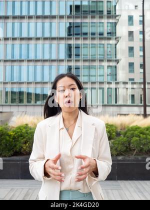 Asiatische junge Geschäftsfrau, die die Kamera anschaut und dabei eine Erklärung macht. Konzept der Geschäftsbotschaft, Videoanruf Stockfoto
