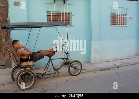 Junger Mann, der sich vor einem Haus auf seinem Fahrrad ausruht, mit einer an die Wand geschriebenen Hommage an den verstorbenen kubanischen Präsidenten Fidel Castro. Stockfoto