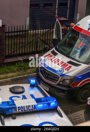 Krakau, Polen - 02. Oktober 2022: Eine europäische Polizei in Uniform, die vor einem Polizeiwagen neben einem Krankenwagen Dienst macht. Tatort und Ermittlungen Stockfoto