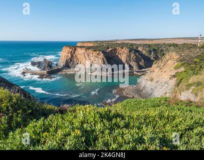 Blick auf den kleinen Fischerhafen von Entrada da Barca von den umliegenden Klippen bei Zambujeira do Mar in Odemira, Portugal. Sonniger Tag, klarer blauer Himmel. Stockfoto