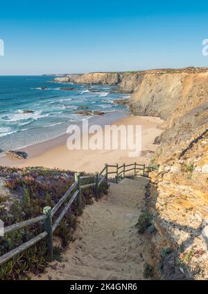 Blick auf den leeren Strand Praia de Nossa Senhora mit Meereswellen, Klippen und Steinen, nassem goldenen Sand und grüner Vegetation an der wilden Küste von Rota Vicentina in der Nähe Stockfoto