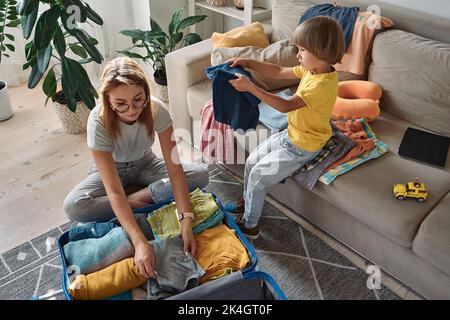 Mutter und Kind packen Dinge zusammen in einen Koffer. Familienumzug, Flucht aus dem Land, geschlossene Grenzen Stockfoto