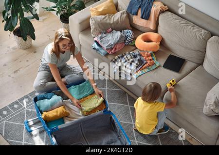 Mutter und Kind packen Dinge zusammen in einen Koffer. Familienumzug, Flucht aus dem Land, geschlossene Grenzen Stockfoto