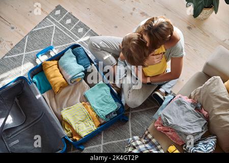 Mutter und Kind umarmen und packen Dinge in einem Koffer zusammen. Familienumzug, Flucht aus dem Land, geschlossene Grenzen Stockfoto