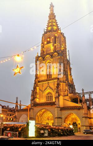 Nachtszene des Berner Münster (Schweizerisch-reformierte Kathedrale) in einer Winternacht, die über dem Berner Weihnachtsmarkt in der Schweiz thront. Stockfoto