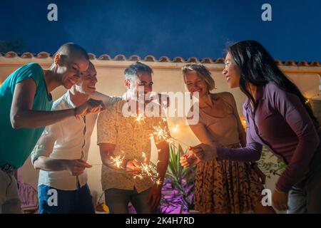 Reife Freunde feiern glücklich mit Funkeln in der Nacht. Fröhliche Menschen feiern in einem Nachtclub im Freien. Stockfoto