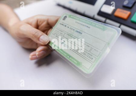 In dieser Fototafel besitzt der Wähler den Wahltitel (Wählerlizenz) - Pflichtposten bei brasilianischen Wahlen mit einer elektronischen Urnenwahlliste im Hintergrund. Stockfoto