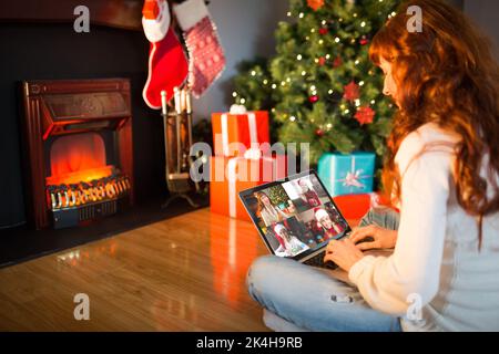 Rothaarige Frau sitzt auf dem Boden mit Laptop an Weihnachten zu Hause im Wohnzimmer Stockfoto