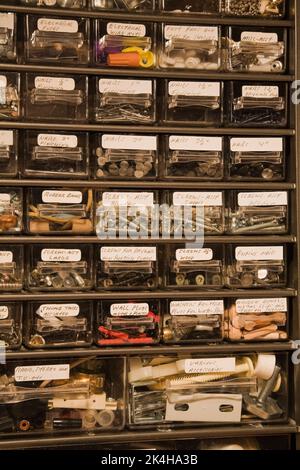 Verschiedene Gegenstände wie Nägel, Schrauben, Ankerdübel, Kunststoffkappen, Gummibänder und mehr in einem Metallschrank mit Kunststoffschubladen aufbewahren. Stockfoto