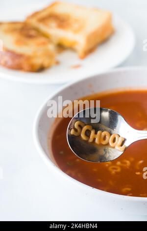 Alphabetsuppe mit dem Wort Schule im Löffel geschrieben. Stockfoto