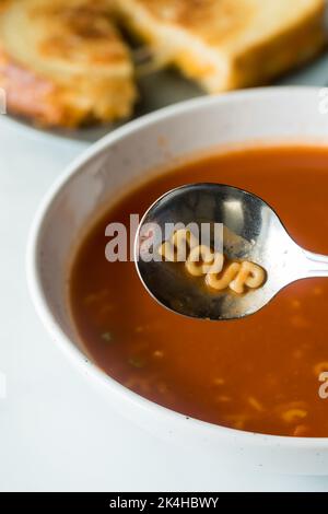 Eine Schüssel gefüllt mit Alphabet Tomatensuppe und das Wort Suppe im Löffel. Stockfoto