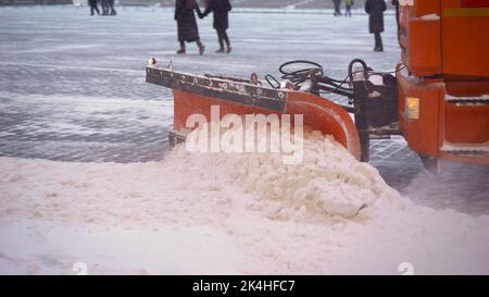 Eine Schaufelnaht reinigt den Gehweg von Schnee. Der Traktor reinigt im Winter den Straßenbelag. Traktor reinigt die Straße vom Schnee. Bagger reinigt Stockfoto