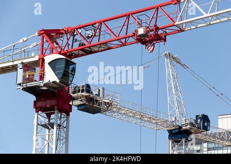 Zwei große, moderne Baufahrkrane, ein roter und ein blauer, sind an einem klaren, blauen Himmelstag aus der Nähe zu sehen. Stockfoto