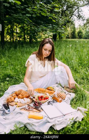 Schöne Frau auf Picknick. Sie lächelt, isst Erdbeeren und genießt den Sommer. Stockfoto