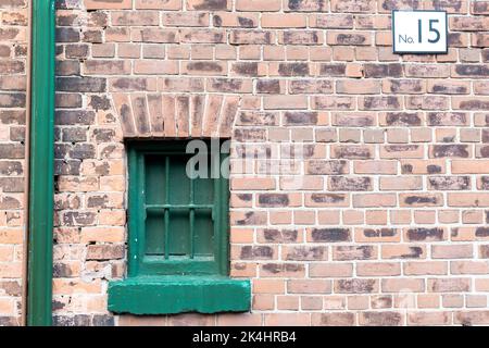 Grünes, kleines Retro-Fenster mit Bars in einem alten Gebäude mit Backsteinmauer Stockfoto