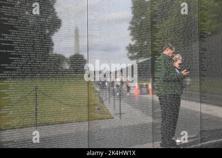 Die Menschen spiegeln sich in den Namen der Gefallenen auf dem schwarzen Granit an der Vietnam Memorial Wall in Washington, DC. Stockfoto