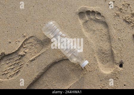 Verschmutzung der Plastikflaschen am Strand mit menschlichen Fußabdruck im Sand. Umweltverschmutzung. Globale Erwärmung. Rette Die Erde. Stockfoto