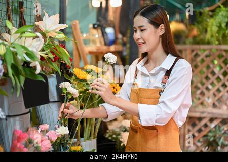 Attraktive junge asiatische weibliche Floristin oder Blumenhändler Besitzer Anordnung Blumen in einer Vase in ihrem Geschäft. Konzept für Inhaber kleiner Unternehmen Stockfoto