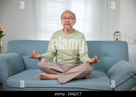 Asiatischer alter Mann praktiziert Yoga und Meditation in Lotusposition und geschlossenen Augen, Lebensstil älterer Mann Lotusposition macht Yoga für das mentale Gleichgewicht Atmung Stockfoto