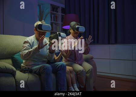 Asiatische Enkelin und Großeltern spielen zusammen spannende interessante Videospiele mit Virtual-Reality-Headsets Wohnzimmer zu Hause, ältere Witz Stockfoto