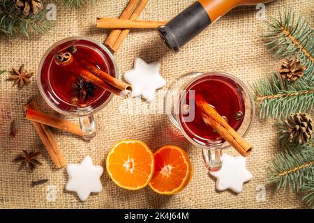Gläser weihnachtlicher Glühwein mit Zimt und Sternanise auf Sacktuch mit einer Weinflasche, Orangenscheiben, weißen Keksen und natürlichem Tannenbaum b Stockfoto