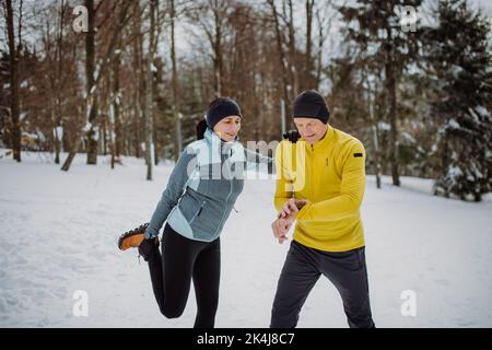 Seniorenpaar macht sich warm und checkt vor der Winterwanderung die Smartwatch im verschneiten Wald. Stockfoto