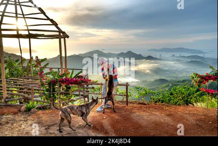 Nha Trang, Khanh Hoa, Vietnam - 23. August 2022: Eine weibliche Touristin spielt mit ihren beiden Haustierhunden auf einem hohen Berg in Nha Trang, Khanh Hoa, Vietnam Stockfoto