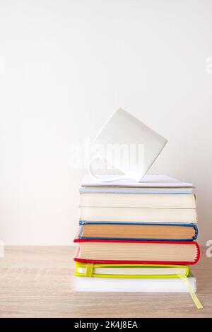 Stapel von Hardcover-Büchern mit einer weißen Tasse Kaffee auf der Oberseite. Stockfoto