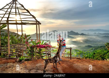 Nha Trang, Khanh Hoa, Vietnam - 23. August 2022: Eine weibliche Touristin spielt mit ihren beiden Haustierhunden auf einem hohen Berg in Nha Trang, Khanh Hoa, Vietnam Stockfoto