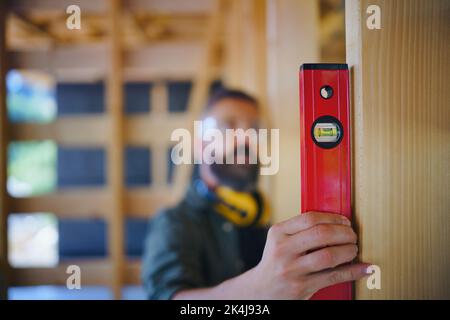 Zimmermann überprüft Holzbretter mit Wasserwaage, diy umweltfreundliche Häuser Konzept. Stockfoto