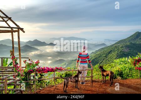 Nha Trang, Khanh Hoa, Vietnam - 23. August 2022: Eine weibliche Touristin spielt mit ihren beiden Haustierhunden auf einem hohen Berg in Nha Trang, Khanh Hoa, Vietnam Stockfoto