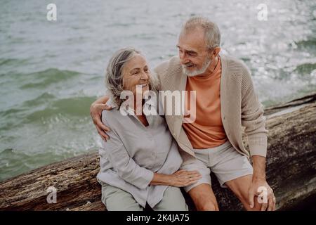 Seniorenpaar sitzt und einen romantischen Moment am Herbstmeer hat. Stockfoto