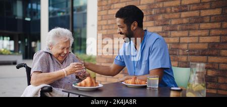 Pfleger beim Frühstück mit seinem Kunden in einem Café. Stockfoto
