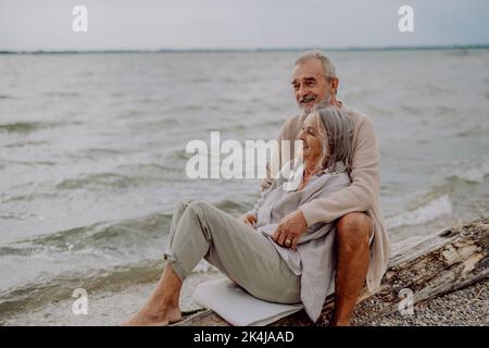 Seniorenpaar sitzt und einen romantischen Moment in der Nähe des Herbstmeers. Stockfoto