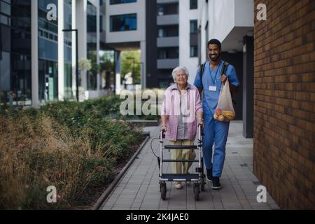 Glücklicher Betreuer, der mit seiner älteren Kundin aus dem Lebensmittelgeschäft zurückkehrte. Stockfoto