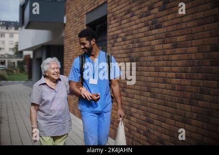 Glücklicher Betreuer, der mit seiner älteren Kundin aus dem Lebensmittelgeschäft zurückkehrte. Stockfoto