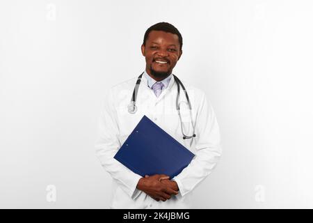 Lächelnder schwarzer bärtiger Arzt in weißer Robe mit Stethoskop hält medizinische Zwischenablage, isoliert auf weißem Hintergrund. Glücklicher Erwachsener schwarzer afrikanischer ameri Stockfoto