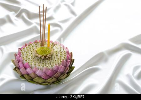 Das rosa Lotusblütenblatt krathong für Thailand das Loy Krathong Festival schmückt mit seinem Pollen, seiner Kronenblume, seinem Räucherstäbchen und seiner Kerze auf einem glatten und welligen Weißklang Stockfoto