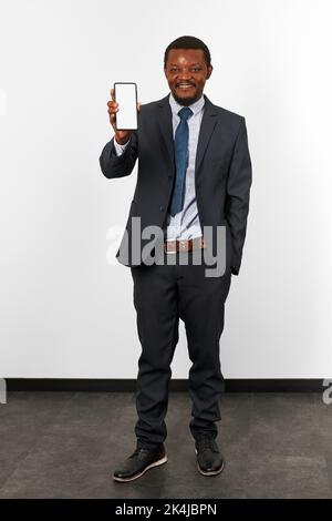Lächelnder afroamerikanischer schwarzer Mann im Business-Anzug mit Smartphone-Mockup in der Hand, weißer Wandhintergrund. In voller Größe Porträt von glücklichen schwarzen Business Stockfoto
