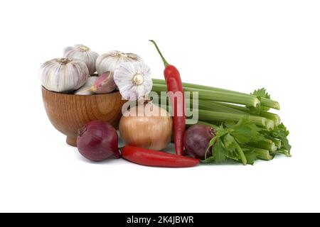 Zwiebeln, Chili und Knoblauchzwiebeln in Holzschüssel vor frischem Sellerie-Stiel, Gewürzen oder Gewürzmotiven Stillleben isoliert auf weißem Hintergrund Stockfoto