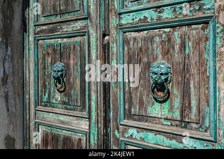 Nahaufnahme einer alten Holztür mit zwei Türknöpfen aus Metall im Löwenstil in Murano, Italien. Stockfoto