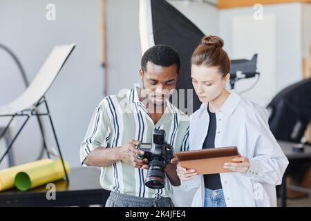 Porträt von zwei jungen Fotografen, die sich im Studio Bilder in der Kamera ansehen Stockfoto