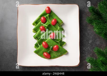 Weihnachtliche, baumförmige Vorspeise aus grünen, dünnen Pfannkuchen auf weißem Teller Stockfoto