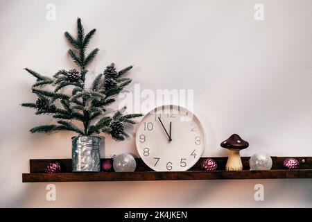 Weihnachtsbaum, weiße Uhr und Dekorationen vor der Holzwand Stockfoto