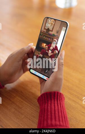 Hände der Frau machen weihnachten Smartphone Video-Anruf mit dem weihnachtsmann in Gesichtsmaske. weihnachten, Festlichkeit und Kommunikationstechnik während covid 19 Stockfoto