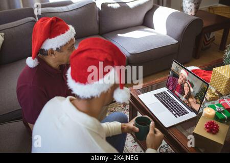 Biracial Vater und erwachsenen Sohn machen Laptop weihnachten Videoanruf mit lächelndem Paar. weihnachten, Festlichkeit und Kommunikationstechnik. Stockfoto