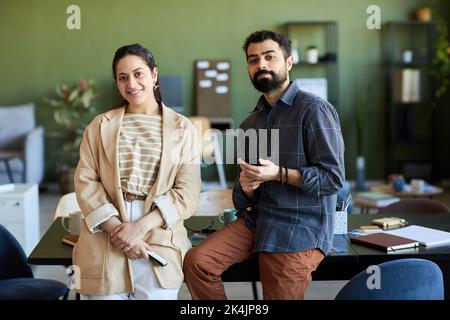 Zwei junge, erfolgreiche Designer oder Angestellte in eleganter Casualwear, die am Arbeitsplatz stehen und die Kamera betrachten Stockfoto