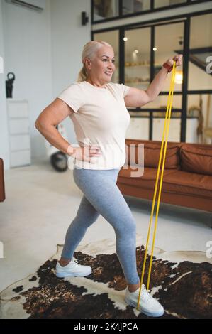 Fröhliche blonde Dame, die das Heim-Workout macht Stockfoto